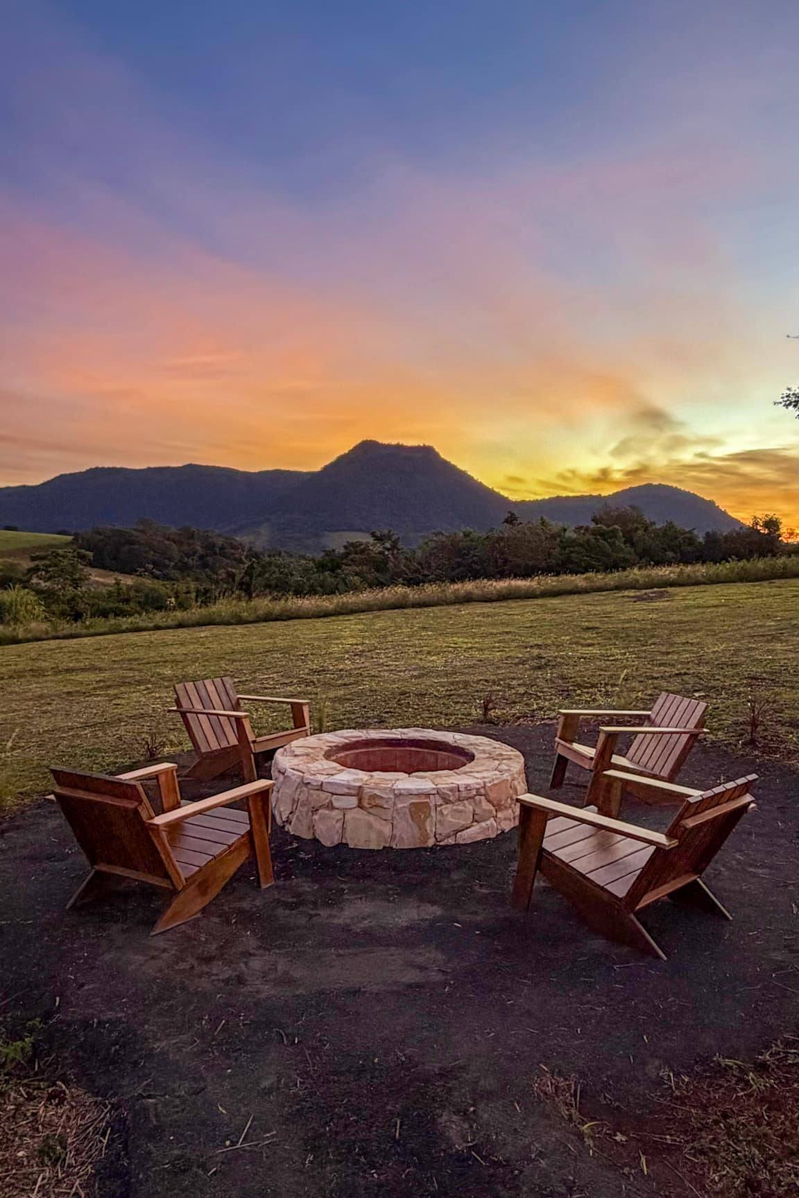 Cuatro sillas de madera alrededor del fogón de piedra, con el Cerro Amor recortado contra el cielo del atardecer.