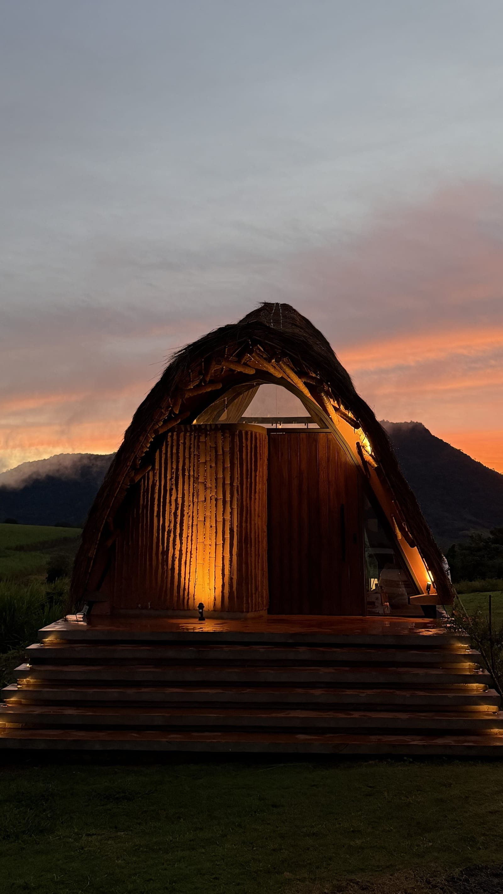El bungalow de paja y tacuara iluminado al atardecer, con la cordillera del Ybytyruzú detrás y el campo abierto delante.