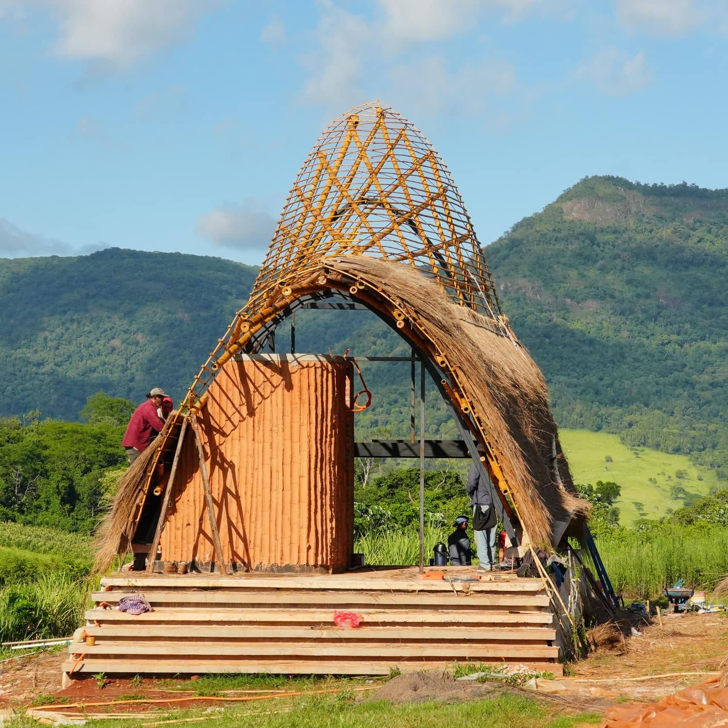 La estructura de tacuara todavía sin cerrar, curvándose sobre la plataforma de madera, con la cordillera detrás.