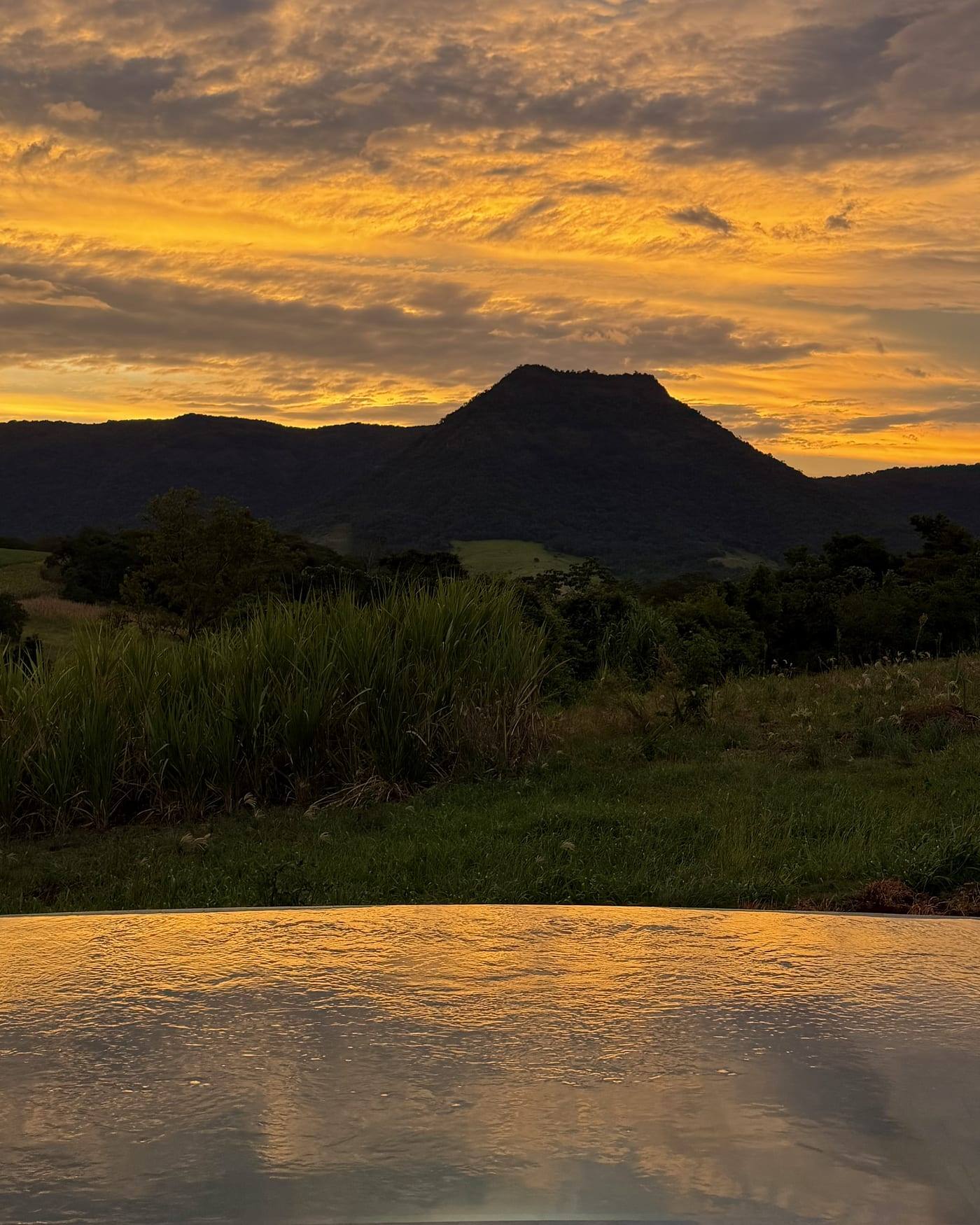 El mismo Cerro Amor al atardecer, negro contra un cielo naranja, y el agua encendida del mismo color.